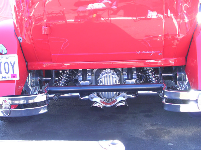 Red hot rod's rear suspension and exhaust pipes. License plate reads 'TOY'
