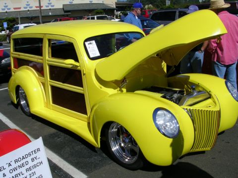 1996 Ford Probe - A bright yellow woody wagon with its hood open, displaying a chrome grille and custom wheels at a car show.