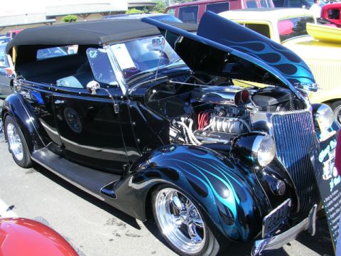 1996 Ford Probe - A custom black convertible hot rod with blue flame graphics is displayed with its hood open, revealing the engine.