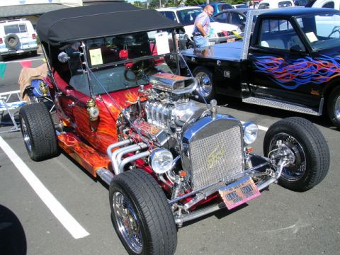 1996 Ford Probe - A custom hot rod with a prominent V8 engine and flame graphics is displayed at a car show.