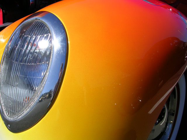 Close-up of a vintage car's headlight with a chrome bezel and a multi-color orange-yellow-red gradient paint job on the fender