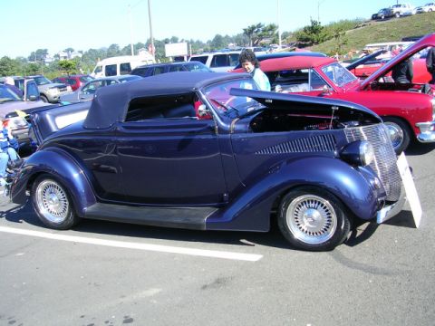 1996 Ford Probe - A dark blue convertible hot rod is parked at an outdoor car show with other vehicles.