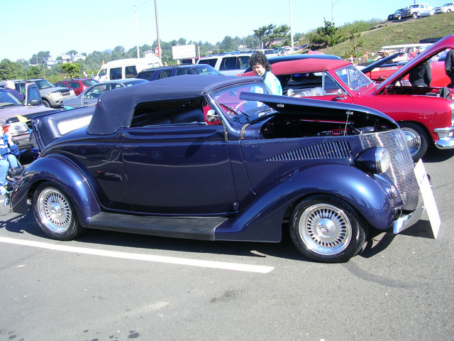 dark blue convertible hot rod parked next to a red car with hood open