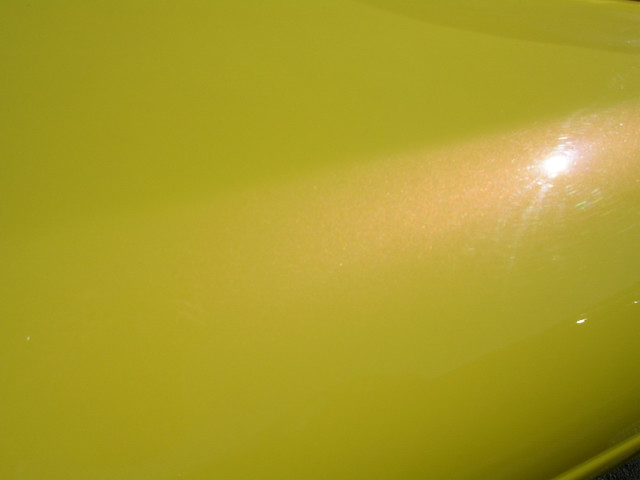 Yellow metallic car body panel with light reflections and minor scratches