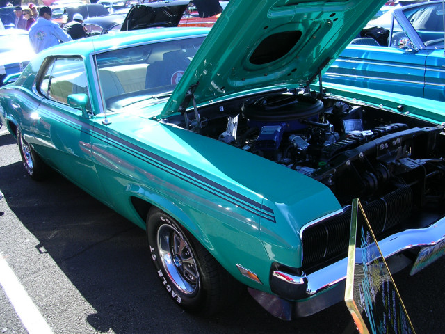 Teal 1970 Mercury Cougar with hood open, showing engine. Black stripes on side. Chrome wheels