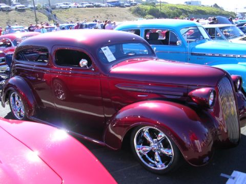1996 Ford Probe - Custom hot rod sedan with chrome wheels at a car show, with other vehicles in the background.