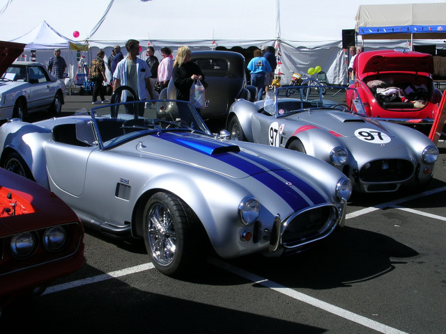 Two silver Shelby Cobra replicas with blue stripes parked next to each other. One has a '97' on its side