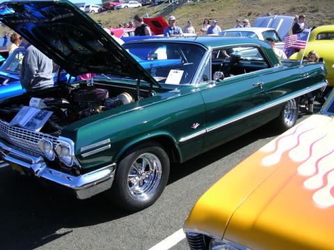 1996 Ford Probe - A classic green Chevrolet Impala is displayed at an outdoor car show with its hood open.
