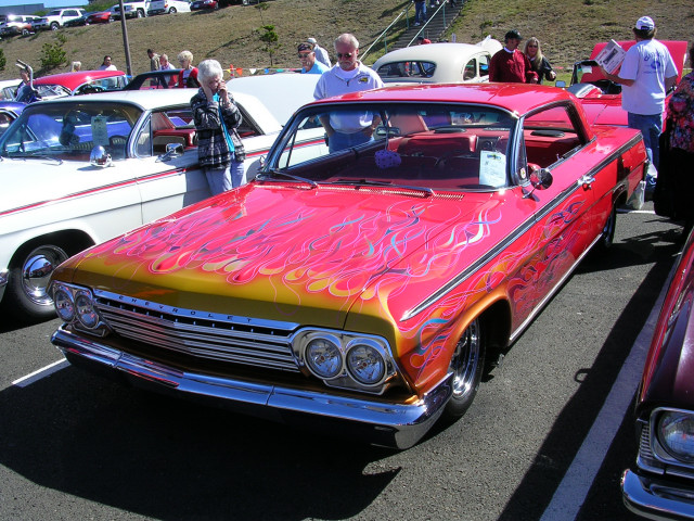 Red and gold Chevrolet Impala with flame graphics, parked at a car show