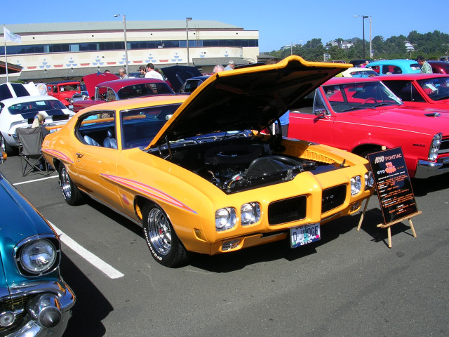 Yellow 1970 Pontiac GTO "The Judge" with hood open at a car show. Other cars visible
