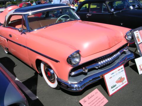 1996 Ford Probe - A salmon and black 1955 coupe with whitewall tires and chrome grille is displayed at a car show.