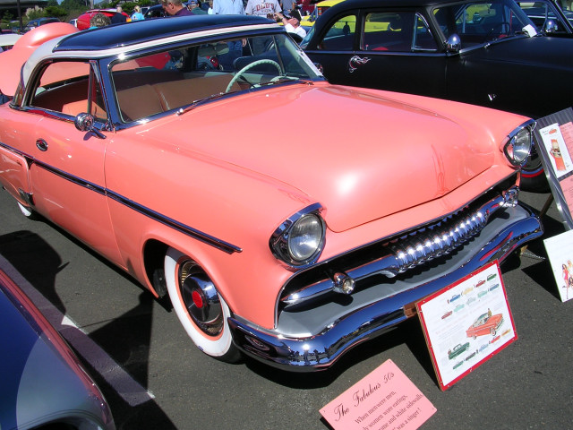 Salmon and black 1955 coupe with whitewall tires and chrome grille, parked at a car show