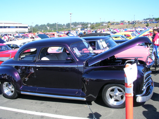 Dark purple coupe with hood open, parked at a car show with other vehicles