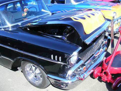 1996 Ford Probe - A black 1957 Chevrolet Bel Air with custom flame decals on the hood is displayed at a car show, with another car visible in the background.