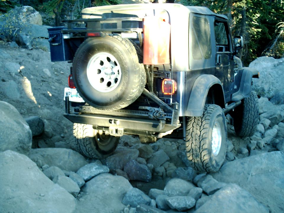 Black Jeep Wrangler TJ on rocky trail with spare tire and gas can