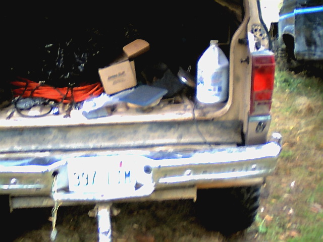 Back of a tan pickup truck with stuff in the bed, another vehicle is visible to the right
