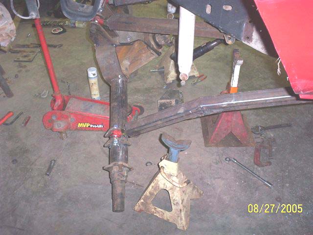Red vehicle frame with suspension components and tools on the floor. Date stamp reads 08/27/2005