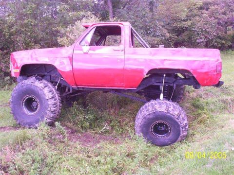 1994 Ford Bronco - This lifted pickup truck has oversized tires and is parked in a grassy, wooded area.