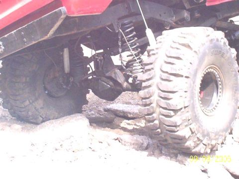 1994 Ford Bronco - Close-up of the rear suspension and oversized tires of a red off-road vehicle navigating rocky terrain.
