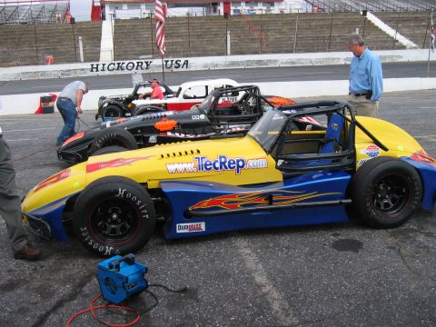 1985 Ford LTD Crown Victoria - Race cars line up at Hickory USA Speedway, with spectators and crew members around.