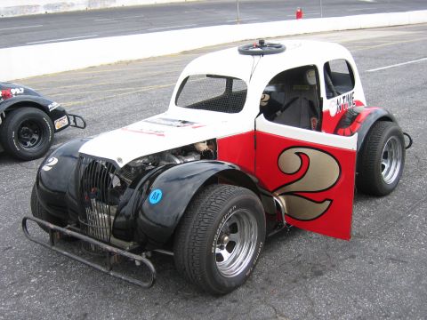 1985 Ford LTD Crown Victoria - A race car with a white top and red sides, displaying the number 2, sits on asphalt with another car in the background.