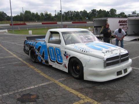 1985 Ford LTD Crown Victoria - A modified Dodge Ram pickup truck, prepared for racing, sits on the asphalt outside a speedway.