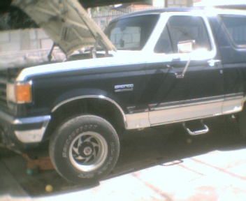 1989 Ford Bronco - A black and white Ford Bronco is parked outside with its hood open, revealing the engine compartment.