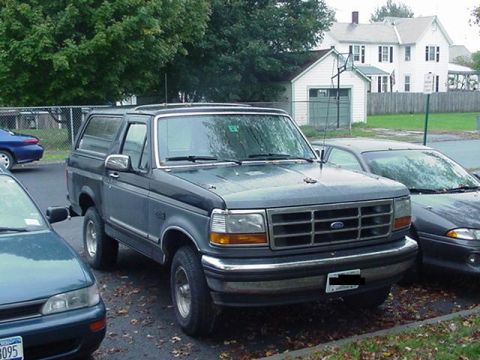 1993 Ford Bronco - A 1993 Ford Bronco is parked in a lot, showing its front grille and headlights.