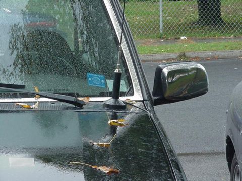 1993 Ford Bronco - A close-up view of a vehicle's side mirror and windshield, with leaves scattered on the hood and water droplets on the glass.