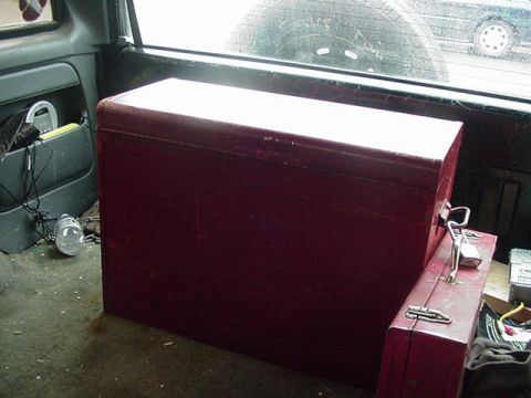 1993 Ford Bronco - The interior of a vehicle shows a large red cooler and a smaller red toolbox, with a spare tire visible through the rear window.