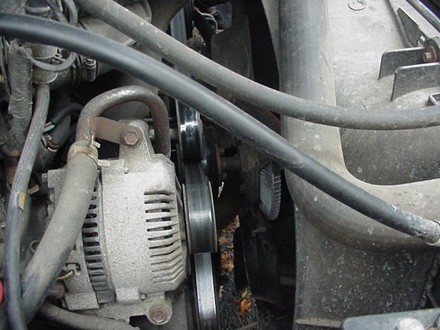 Alternator and pulley system in an engine bay, with hoses and wiring visible