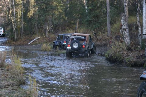 2003 Jeep TJ - Multiple Jeeps navigate a muddy off-road trail with water obstacles.