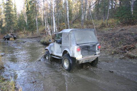 2003 Jeep TJ - A gray Jeep CJ-7 navigates a muddy trail with another Jeep in the distance.
