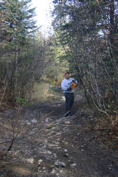 2003 Jeep TJ - A man stands on a dirt path in a wooded area, holding a yellow chainsaw.
