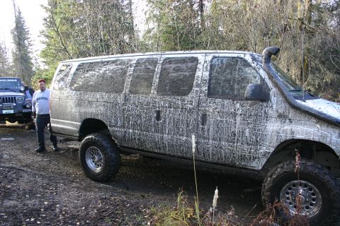 2003 Jeep TJ - A white van, heavily coated in mud, is parked next to a Jeep in a wooded area.
