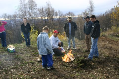 2003 Jeep TJ - People are standing and sitting around a campfire in a wooded area.