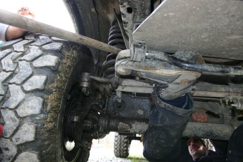 2003 Jeep TJ - Mechanic works on the undercarriage of a vehicle, focusing on the suspension and tire assembly.