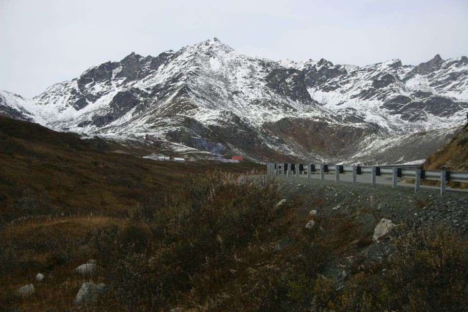 Mountain landscape with snow-capped peaks, brown hills, and a guardrail along a road