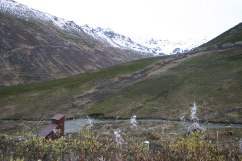 2003 Jeep TJ - A yellow tractor is parked near a small structure in a vast mountain valley, with snow-dusted peaks in the background.