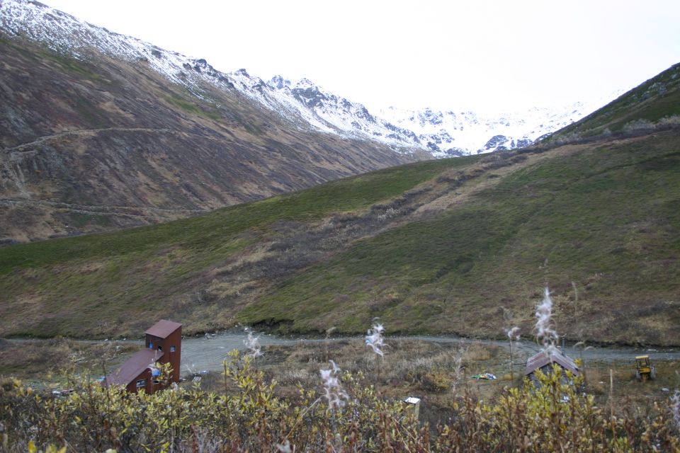 Yellow tractor near a small building in a mountain valley with snow-capped peaks