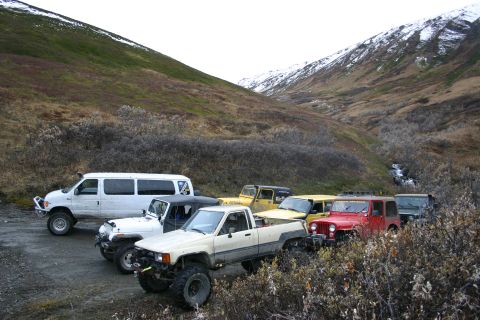 2003 Jeep TJ - A convoy of off-road vehicles is parked in a valley, with a stream visible in the background.