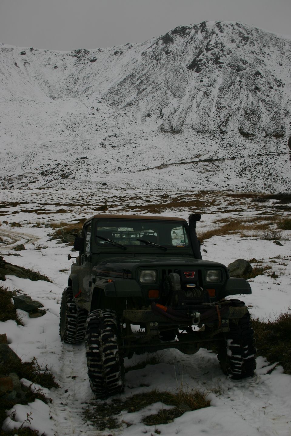 Dark green 2003 Jeep TJ with large tires and snorkel in snowy mountains