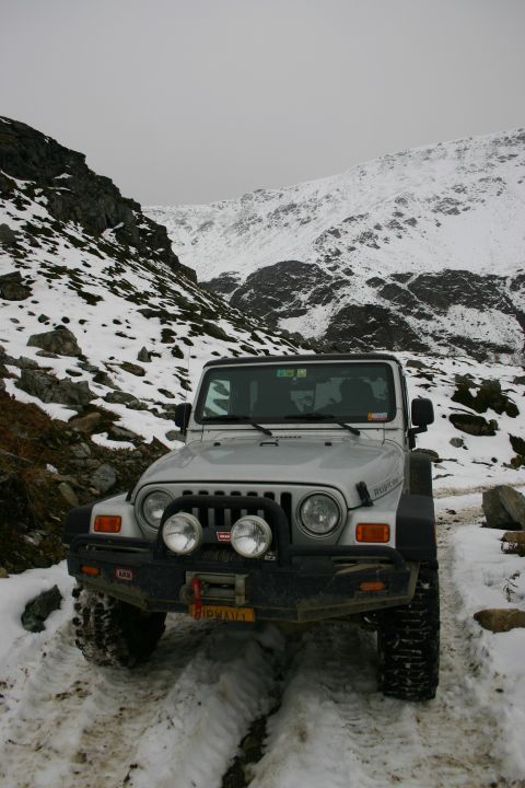 2003 Jeep TJ - Silver 2003 Jeep TJ navigating a snowy mountain path with snow-capped peaks in the background.