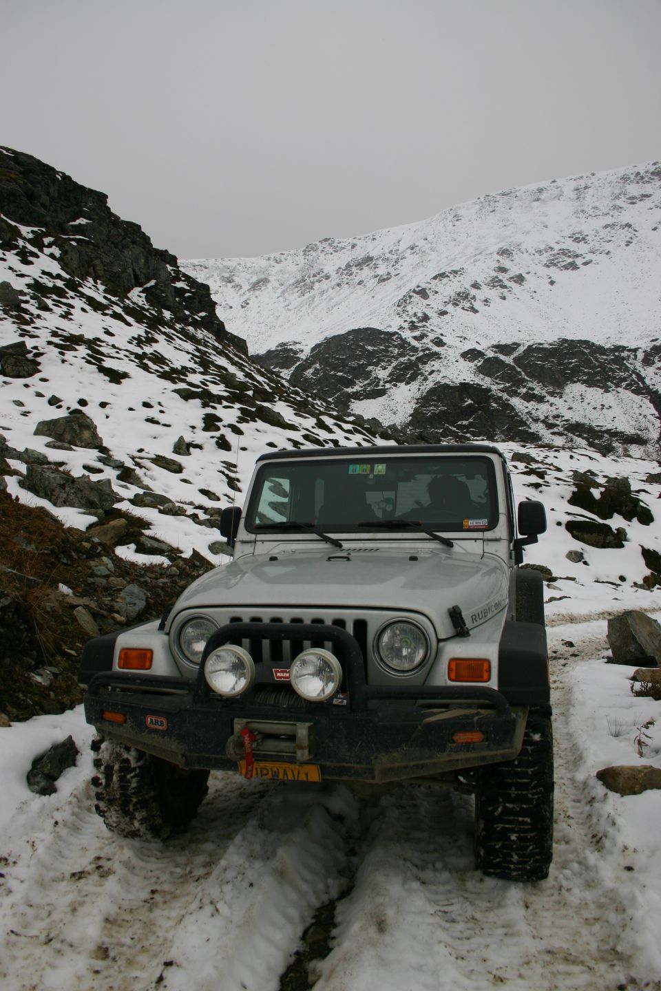 Silver Jeep TJ parked on a snow-covered mountain trail, front view