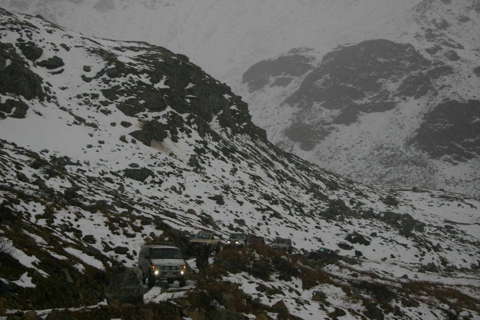 Vehicles parked on dirt road across a snow-covered rocky mountain bowl