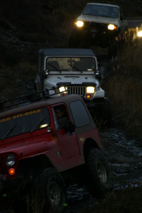 2003 Jeep TJ - Three Jeeps drive in formation on a dark, muddy off-road trail.