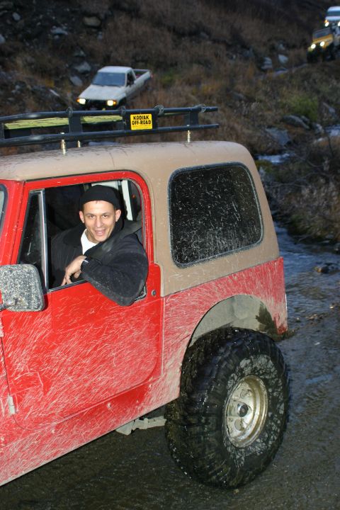 2003 Jeep TJ - A red 2003 Jeep TJ navigates an off-road trail with other vehicles in the background.