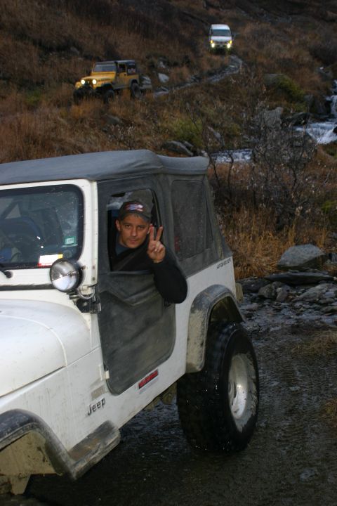 2003 Jeep TJ - Driver of a white Jeep TJ signals peace while off-roading with two other vehicles in mountainous terrain.