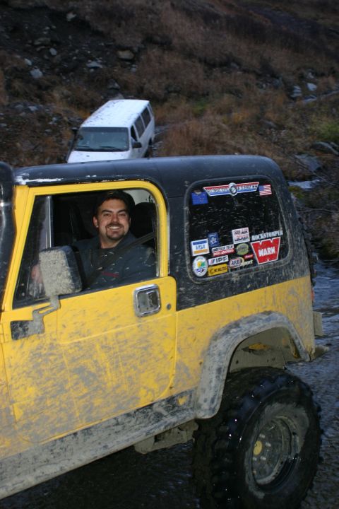 2003 Jeep TJ - A yellow Jeep Wrangler TJ is on a muddy trail with a white van in the background.