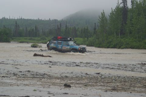 2003 Jeep TJ - Jeep Cherokee XJ navigates a muddy river crossing in a wooded, overcast landscape.